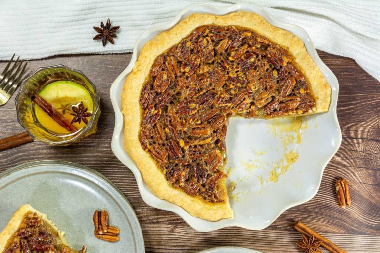 Bourbon pecan pie with a slice removed, served with spiced apple drink on a rustic table.