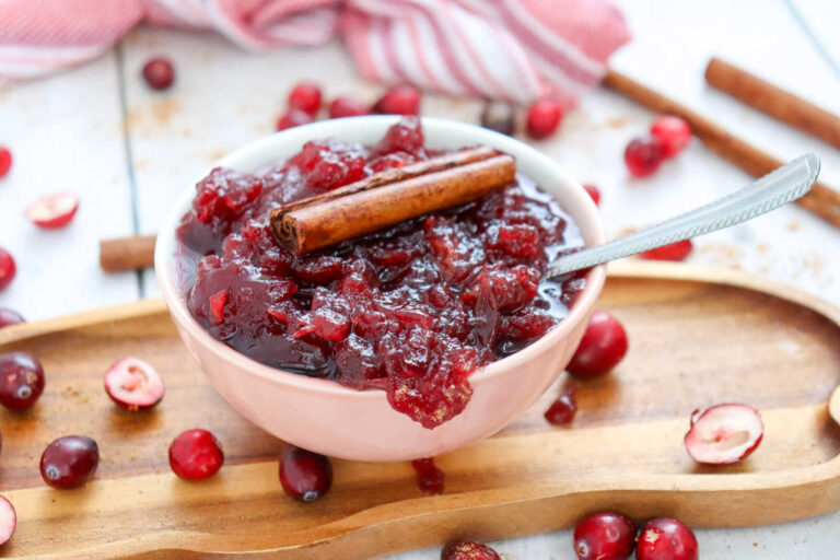 Homemade cranberry sauce recipe with cinnamon stick in a bowl and fresh cranberries.
