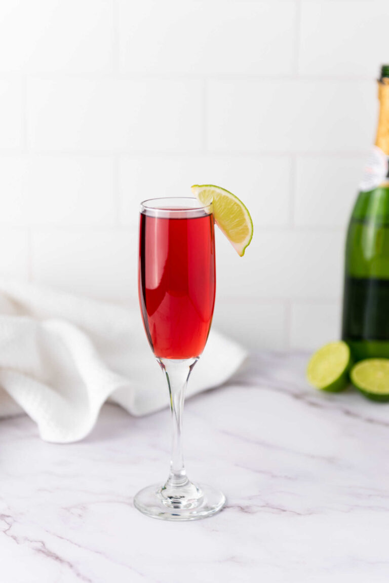 Cranberry mimosas in a champagne flute with lime garnish on a marble surface